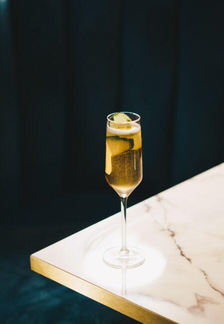 A single, filled champagne glass on a marble table with green background