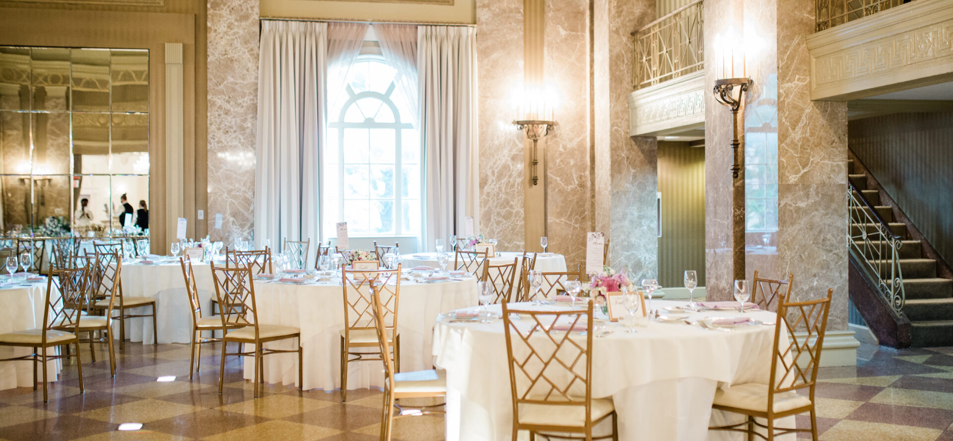 Set tables within a golden, marble walled ballroom