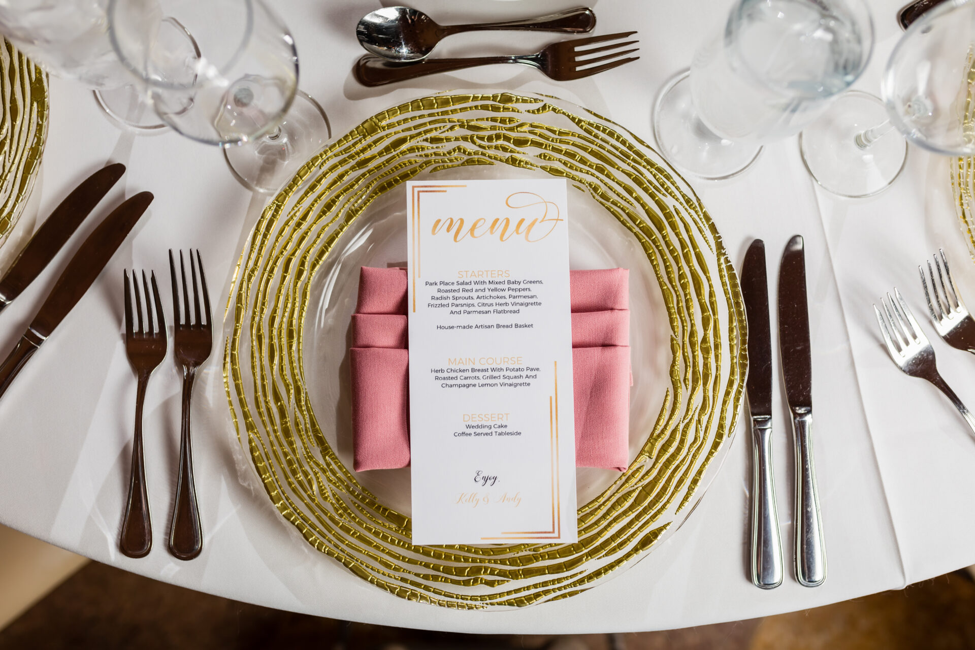 Wedding menu card atop a pink napkin and gold placemat
