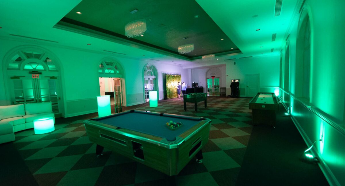 Green lit lounge room at a venue with pool table and shuffleboard