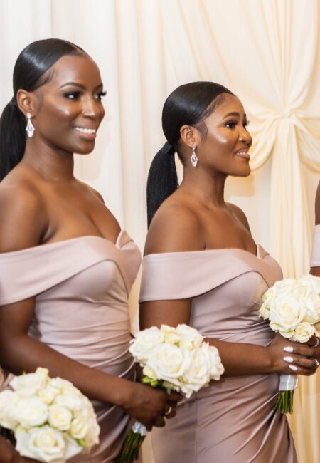Two bridesmaids in light pink dresses holding white flowers, gazing towards the off-screen bride