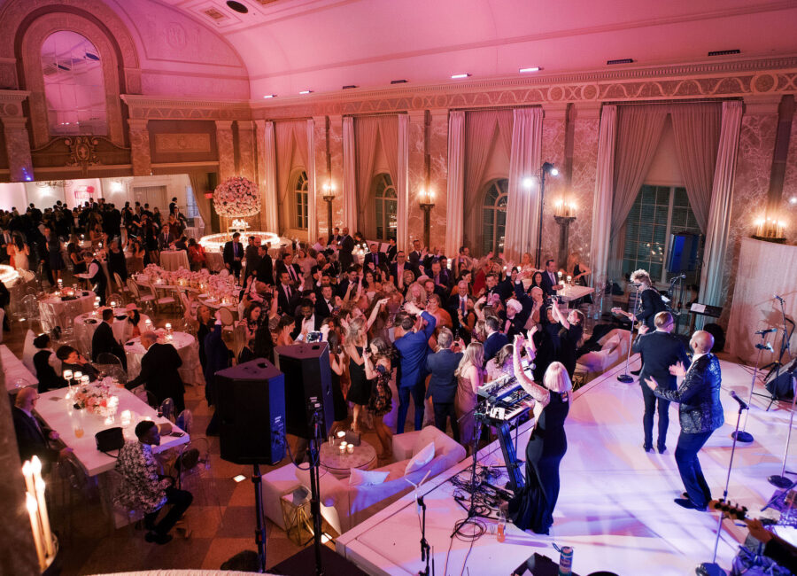 Wedding band playing in front of a crowd at a wedding in a spacious ballroom