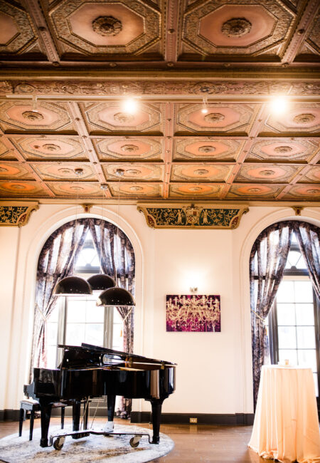 Black grand piano within a high-ceilinged, mid century wedding venue