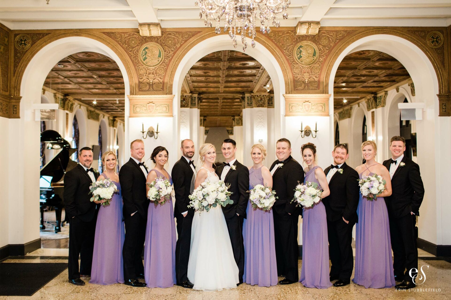 12 person wedding party in elegant room, with suited men and purpled-dressed women rotating and wedding couple in the center