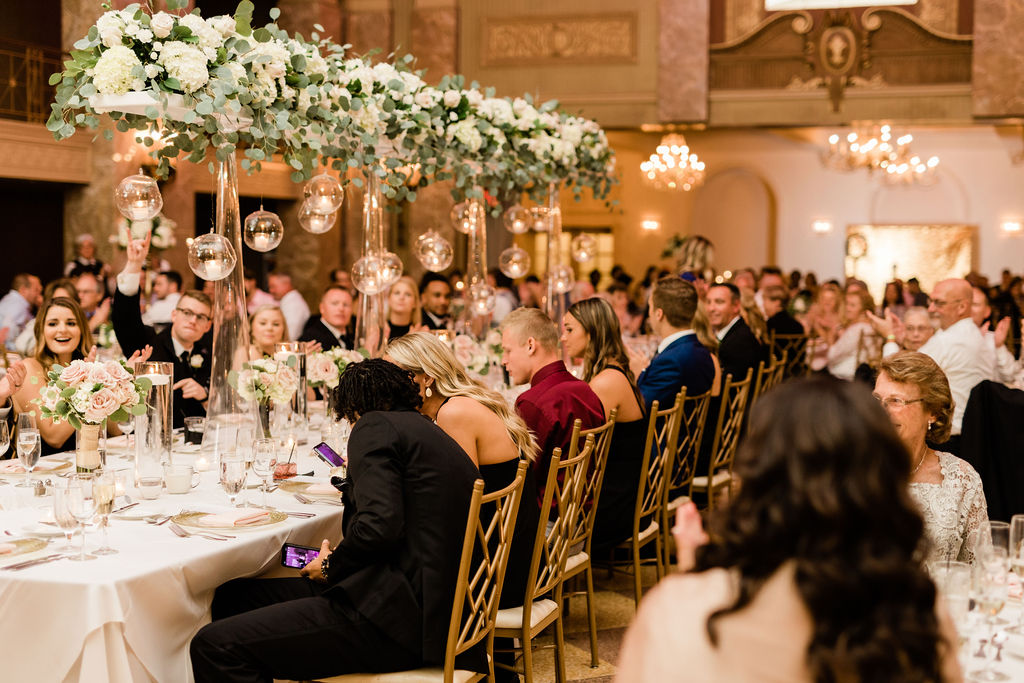 Briday party seated at the long, head wedding table with an ornate, elevated floral and glass centerpiece